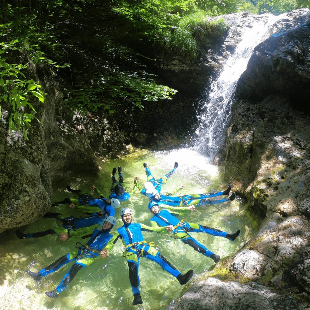 A happy group of friends in their neoprene suits makes a floating star while Bovec canyoning.