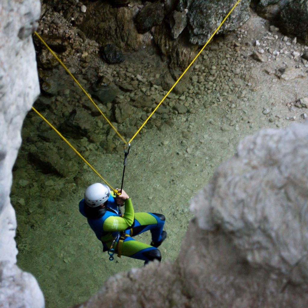 A canyoneer in a wetsuit is ziplining from the top of a waterfall in Bovec.