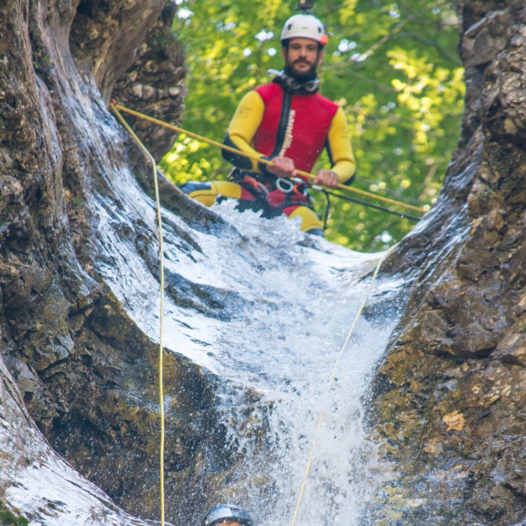 Canyoning guide Matej lowering a girl down Parabola waterfall.