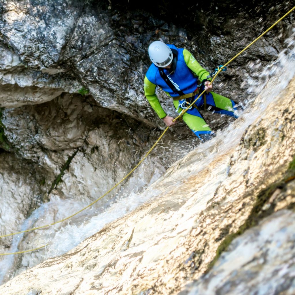 A man in a neoprene suit is learning how to rappel down the slippery waterfalls in Bovec.